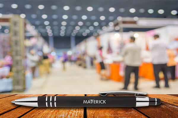 Un ambassadeur de marque d’une entreprise offrent des stylos publicitaires comme goodies aux personnes intéressées sur le stand d’un salon.